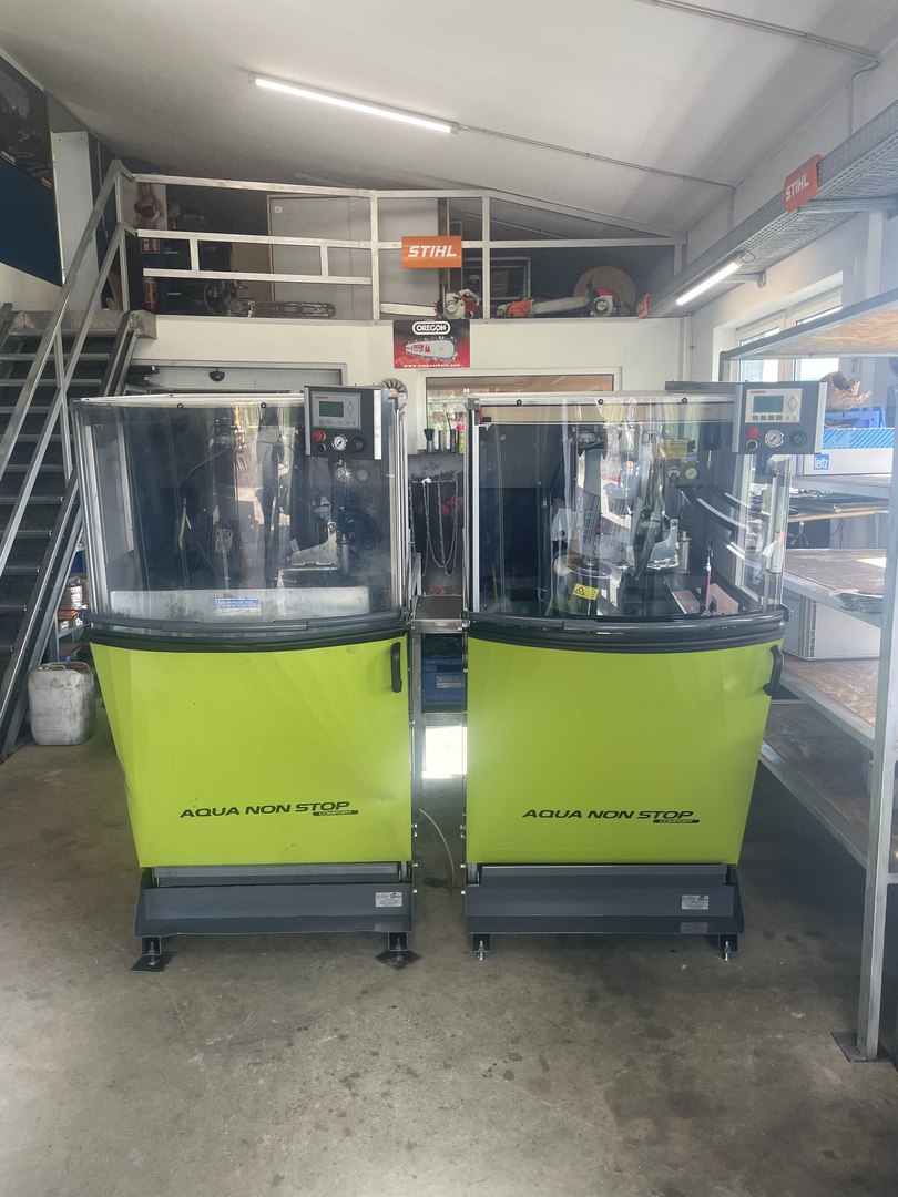 Zwei hellgrüne Schleifautomaten vom Typ Aqua Non Stop Comfort in der Werkstatt, im Hintergrund STIHL- und OREGON-Schilder